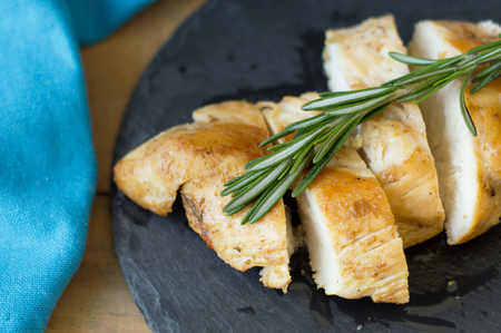 Top view of cooked chicken slices with fresh rosemary on black slate board and blue kitchen towelの写真素材