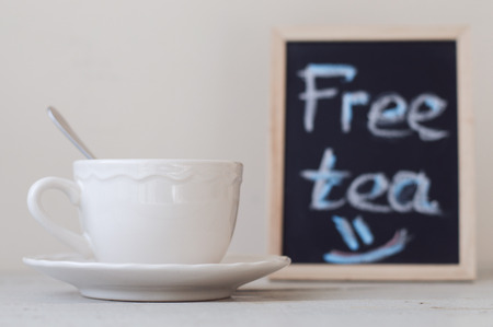 White cup with tea standing near blackboard sign with promotion "Free Tea". Hot beverage and chalk board with handwritten text on gray backgroundの写真素材