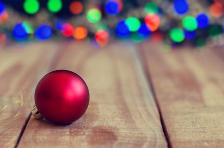 Christmas card with red ball on wooden background and colorful blurred lights. Christmas and New Year atmosphereの写真素材