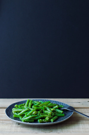 Portion of freshly cooked green beans with sesame seeds served with a metal fork on wooden table. Black backgroundの写真素材