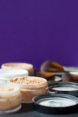 Vertical photo of make up mineral powder of beige and white colors and make up brushes on purple backgroundの写真素材