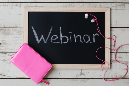 Webinar concept. Blackboard with handwritten text "Webinar", pink notebook and earphones on wooden background, top viewの写真素材