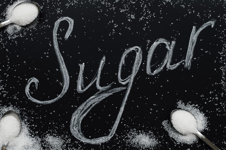 Sugar eating concept. Refined white sugar in small spoons on black background. Food lettering. The word "Sugar"の写真素材
