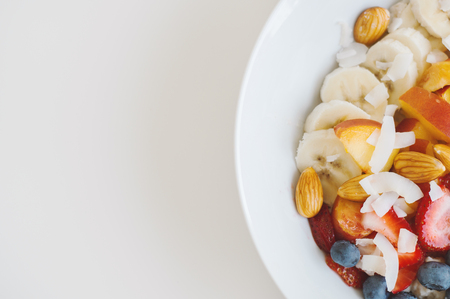 White plate with oats, banana, almond, blueberry, peach and coconut flakes. Healthy breakfast. Cope space, top viewの写真素材