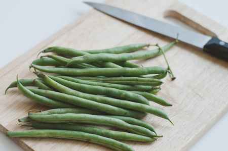 Fresh raw green beans and a big knife on wooden cutting board. Food ingredient