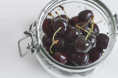 Glass jar with fresh cherries on white table. Dark berries. Summer season fruitsの写真素材