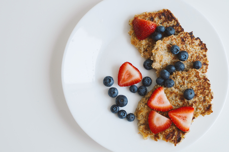 Brown pancakes from whole grain oats served with fresh bluberry and sliced strawberry on white...