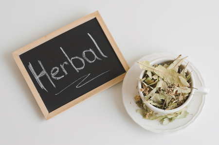 Dried lime flowers in a white cup and blackboard with the text "Herbal", top view. Herbal tea. Herbal medicine conceptの写真素材