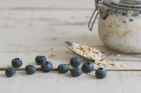 Blueberries, spoon with whole oats and jar witj homemade overnight oatmeal on wooden tableの写真素材