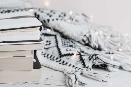 Woolen knitted blanket, lights for home decor and a pile of books, diaries and planners on wooden table. Reading concept. Cosy and comfortable atmosphereの写真素材