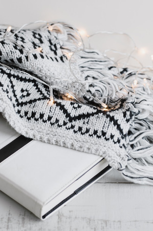 Vertical photo of white book (or diary, notebook, day planner), lights and warm knitted blanket. Reading conceptの写真素材