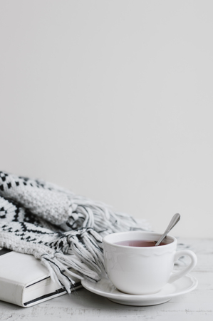Vertical background with white cup of red tea, book and knitted blanket on wooden table, copy space. Hygge concept. Tea breakの写真素材