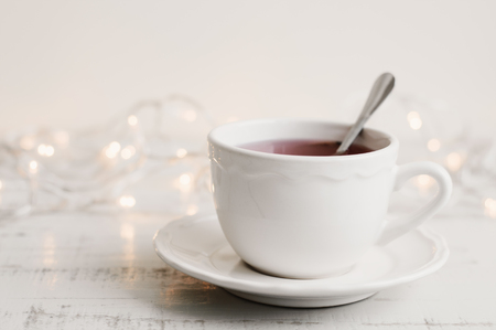 Cup of red hibiscus tea in a white mug, yellow lights on background. Herbal drink on wooden table. Tea breakの写真素材