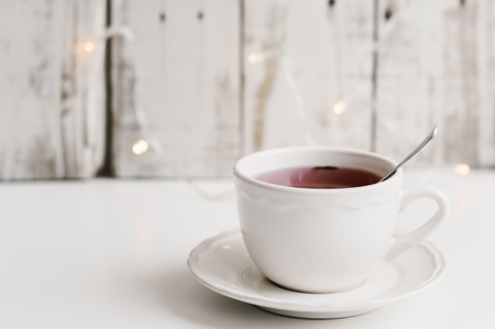 Red tea in a small white cup on white table, wood and small yellow lights as backgroundの写真素材