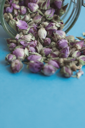 Vertical photo of herbal tea. Dried rose buds in a jar on blue backgroundの写真素材