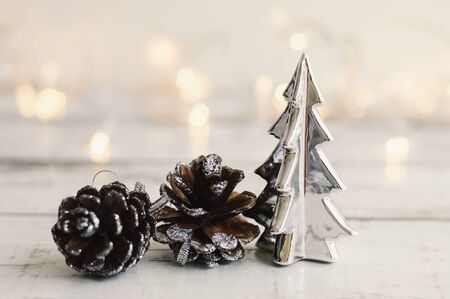 Mini christmas tree of silver color and pine cones on wooden table, Christmas lights as background. Winter decorの写真素材