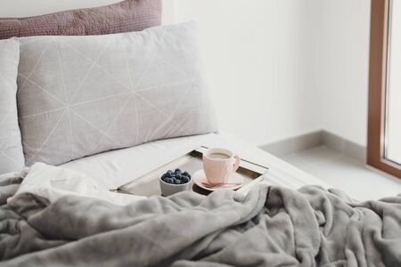 Breakfast in bed concept. Coffee with milk in a pink cup and fresh blueberry on a metal tray. Eating in bedroom. Morning coffeeの写真素材
