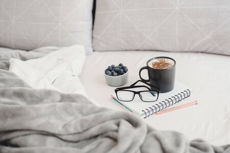 Morning coffee in bed. Working or Studying from home. Coffee, blueberries, glasses, pen and note book. Work from homeの写真素材