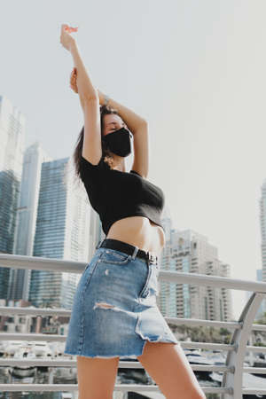 Young female model wearing t-shirt, skirt and reusable protective face mask and posing at city street. Casual outfitの写真素材