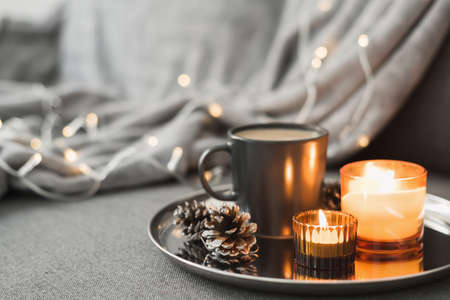Two burning aroma candles, coffee in a black mug and decorative pine cones served on a round metal tray. Cozy atmosphere. Hygge conceptの写真素材