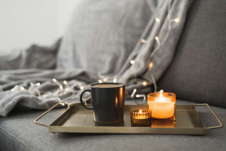 Hot coffee and two burning aroma candles on a metal tray, cozy atmosphere at homeの写真素材