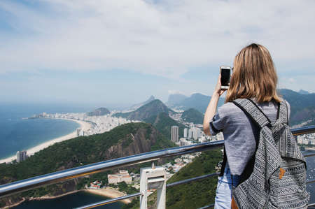 Rio de Janeiro; Brazil - February, 12, 2019: Female tourist taking a mobile photo of Copacabana beach from the observatory deck at Sugarloaf mountain in Rioのeditorial素材