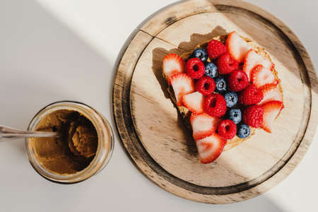 Peanut butter toast with strawberry, raspberry and blueberry on wooden board and jar with creamy peanut butter. Breakfast foodの写真素材