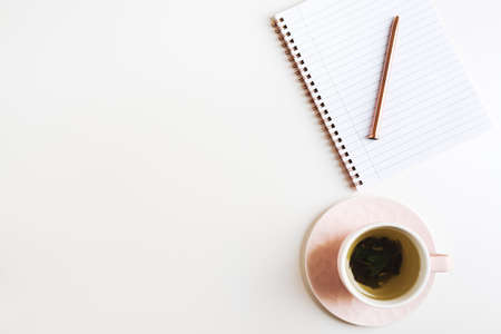 Minimal flat lay with green tea in a pink cup, notepad with empty pages and metal pen on white table, space for textの写真素材
