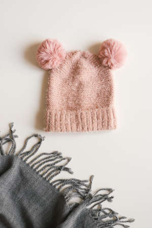 Handmade knitted hat of pink color with two funny pompoms and woolen scarf of gray color on white...