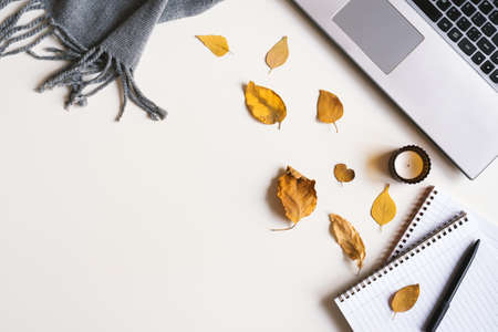 Home office desk with laptop, candle, notebooks, pen, blanket and small dried leaves. Autumn season...