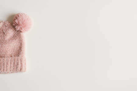 Handmade woolen knitted hat with pompom of pink color on white background, top view, space for text....