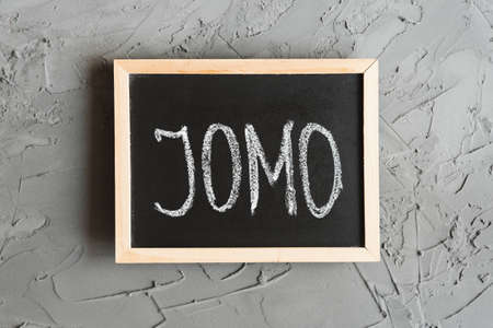 JOMO concept. JOMO means Joy of Missing Out. Acronym written on a small blackboard, concrete wall as backgroundの写真素材
