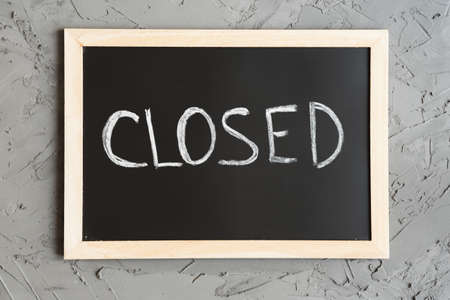 Closed sign board. Word "Closed" written on a blackboard with wooden frames, concrete wall as backgroundの写真素材