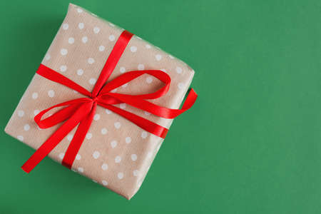 One gift box wrapped in craft polka dot paper with red ribbon on green background, top view, copy space. Eco friendly Christmas present wrapping ideaの写真素材