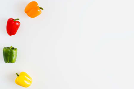 Simple background with colorful bell peppers on white kitchen table. Capsicum of orange, red, green...
