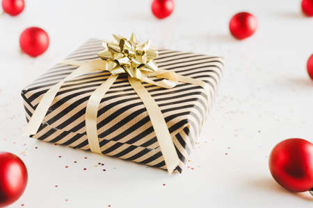 Gift box wrapped in kraft paper with golden ribbon, Christmas balls and small glitters on white...