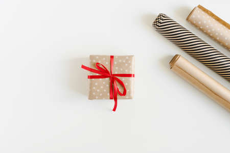 Gift box wrapped in polka dot kraft paper with red ribbon and paper rolls on white table, top view. Eco-friendly Christmas gifts wrapping ideaの写真素材