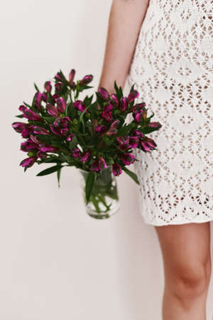 Woman in a white handmade dress holding Alstroemeria flowers bouquet in a transparent vaseの写真素材