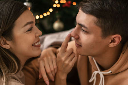 Portrait of a young man and woman sitting near Christmas tree and having funの写真素材