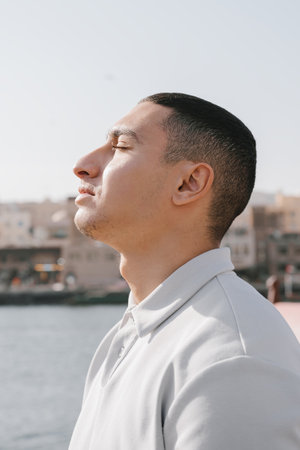 Portrait of a young arab male captured outdoors with his eyes closed. Generation Z man standing near...