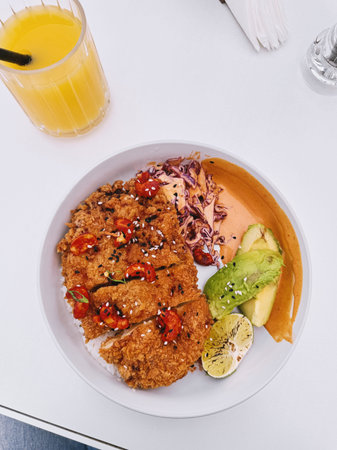 Overhead view of crispy breaded chicken served with rice, avocado, cabbage, spicy cashew topping and sauceの写真素材