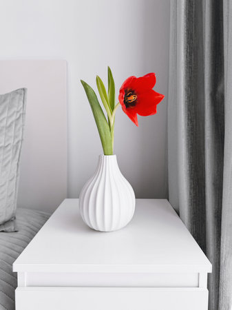 Red tulip in a white ceramic vase on a bedside table. Bedroom interior. Calm lifestyle and home decor conceptの写真素材