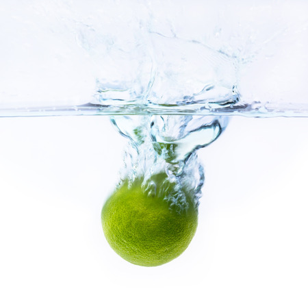 green lemon falling into the water with splash and little air bubbles