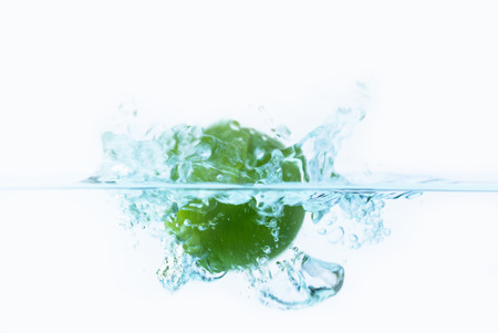green lemon falling into the water with splash and little air bubblesの写真素材