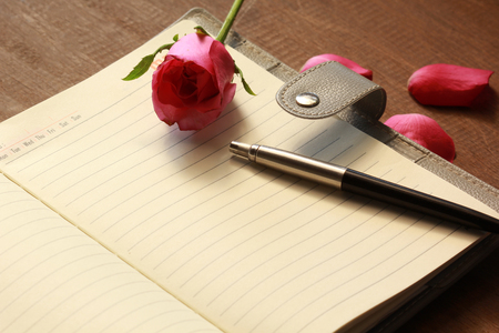 The book with pink rose and pen on wood table.の写真素材