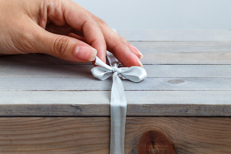 female hand unties the ribbon on gift wooden box.の写真素材