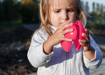 little girl playing with a red plastic heart. she holds it in her hands.の写真素材