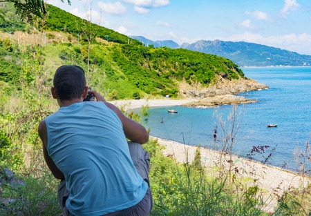 view from the back, male photographer takes a wild seashore.の写真素材
