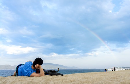 Men with his bicycle lying on a beach.の写真素材