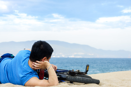 Men with his bicycle lying on a beach.の写真素材